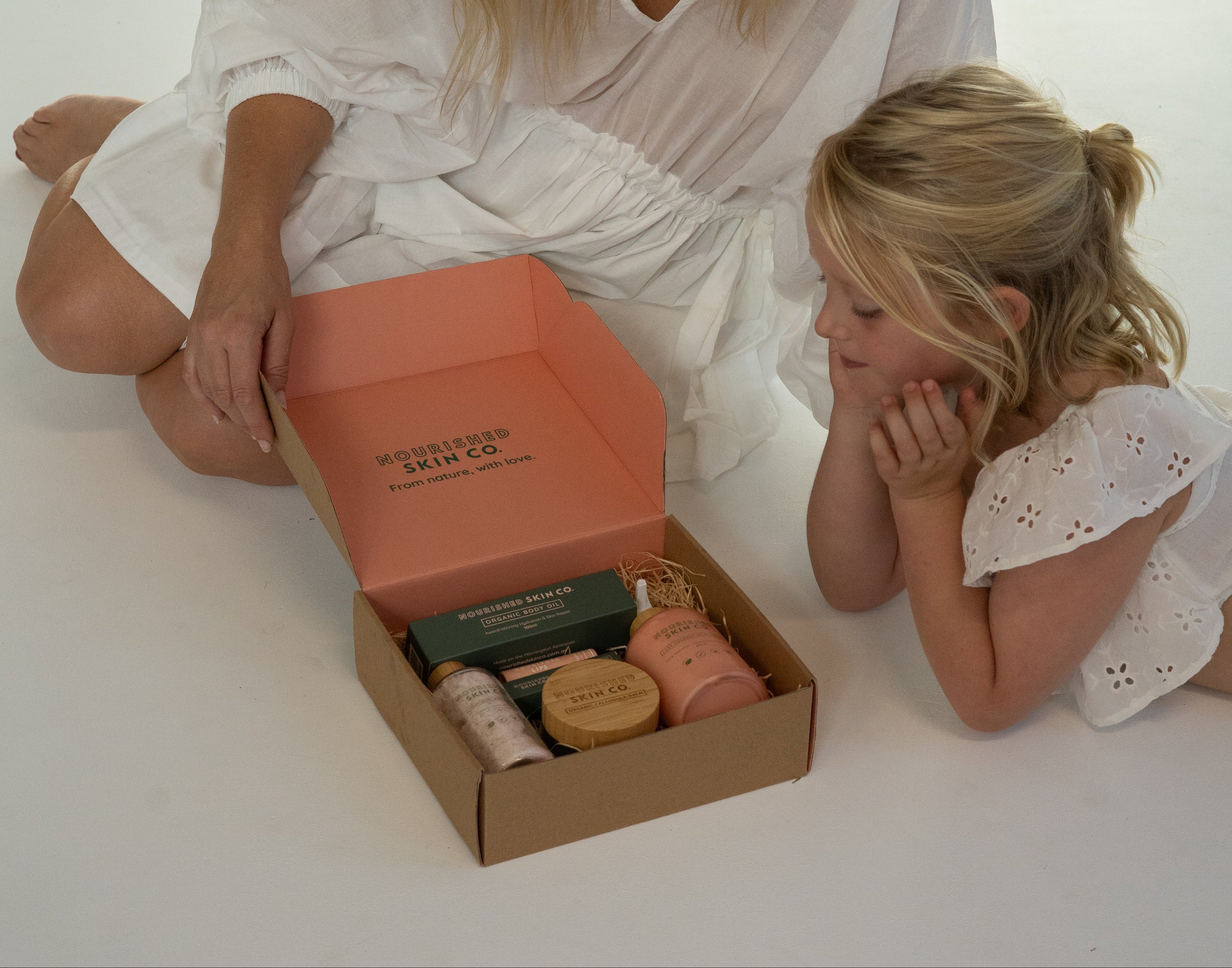 Woman and child sitting on a white floor with a box of products.